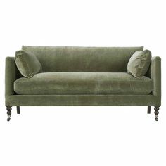 a green velvet couch with two pillows on the armrests and one pillow sitting on top of it