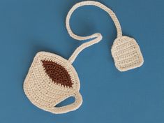 a crocheted coffee cup and saucer set on a blue surface with a white cord