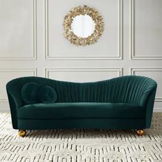 a green velvet couch in front of a white wall with a circular mirror on it