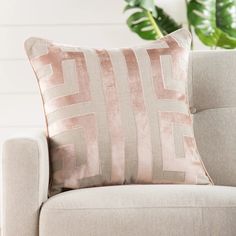 a beige couch with a pink pillow on it and a green plant in the background