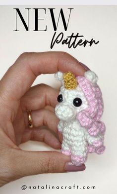 a hand holding a small crocheted white and pink poodle with a gold crown on it's head