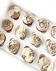 twelve cupcakes with white frosting in a box on a table top, ready to be eaten