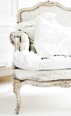 an old chair with white sheets and pillows on it