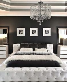 a white bed sitting under a chandelier next to two pictures on the wall