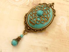 This large, unique brooch is a beautiful accessory that can be worn in many ways: on blouses, sweaters, vests, jackets, scarves, cases, hats, backpacks, bags, bridal bouquets and much more. The brooch consists of a solidly crafted jewelry setting made of bronze-colored metal and a large turquoise cabochon, which is also decorated with an ornate metal ornament and another small turquoise cabochon. A jewelry pendant with turquoise beads is attached to the bottom of the brooch. The brooch, including the pearl pendant, measures 8.3 L x 3.5 W cm. A MATCHING HAIR CLIP YOU WILL FIND IN MY SHOP- Blue Cabochon Brooches For Wedding, Unique Cabochon Brooches For Weddings, Elegant Large Pendant Brooches For Gifts, Elegant Large Pendant Brooches As Gifts, Unique Wedding Cabochon Brooches, Wedding Brooches With Cabochon Pendant, Wedding Brooch With Cabochon Pendant, Wedding Pendant Brooches With Cabochon, Turquoise Cabochon Brooch For Gift