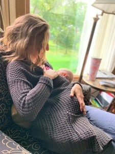 a woman sitting on a couch holding a baby in her lap and looking out the window