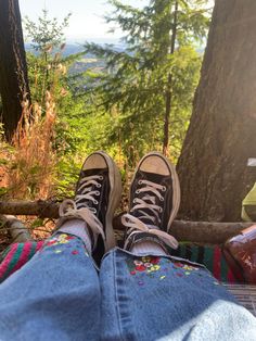 someone's feet with sneakers on sitting in the woods