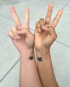 two people with matching wrist tattoos making the peace sign and cat on their arm,