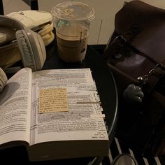 an open book sitting on top of a table next to a cup of coffee and headphones