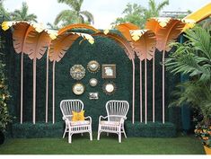 two white chairs sitting next to each other in front of a green wall with palm trees