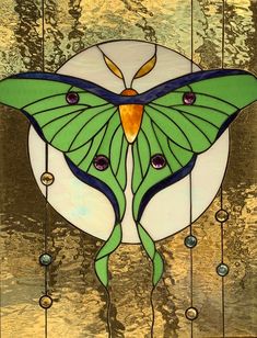 a stained glass window with a green butterfly on it's face and beads hanging from the side