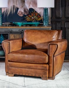 a brown leather chair sitting in front of a painting on the wall next to a lamp