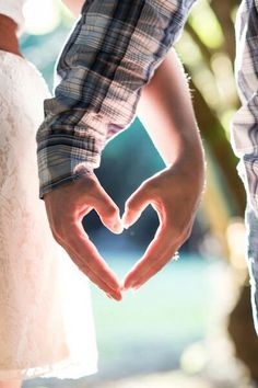 a man and woman holding hands making a heart shape with their hands while standing next to each other