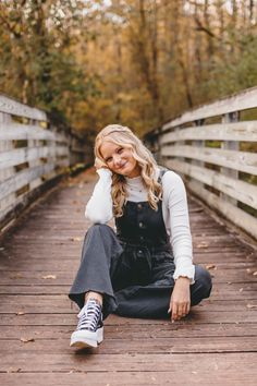 a woman sitting on the ground in front of a bridge with her legs crossed and smiling