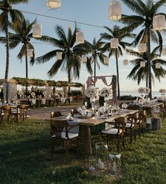 an outdoor wedding reception setup with palm trees and hanging lanterns in the background at sunset