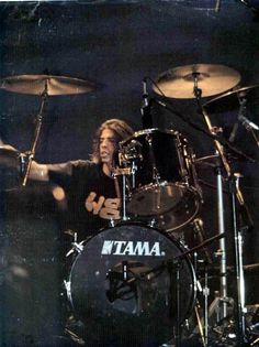 a man with long hair playing drums on stage