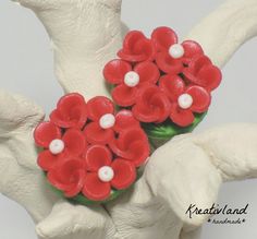 two white hands holding red flowers on top of each other with pearls in the middle