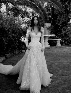 a woman wearing a wedding dress standing in the grass with her hands on her hips