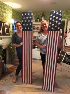 two women holding american flags made out of cardboards in a room with green wallpaper