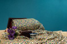 a purple flower sitting on top of a bed next to a wooden box filled with confetti