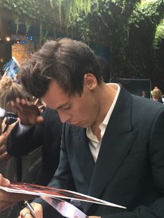 a man in a suit signing autographs for fans at an event with other people