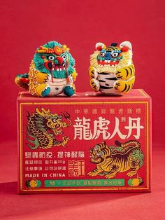 two small figurines sitting on top of a box with chinese writing in it