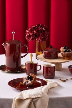 a table topped with plates and cups filled with desserts next to a red wall