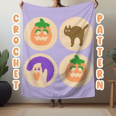 a woman holding up a purple towel with four pumpkins and cats on it in front of a plant