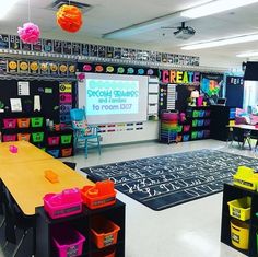 an empty classroom with lots of desks and colorful bins on the floor in front of a projector screen