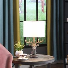 a deer head lamp sitting on top of a table next to a pink chair in front of a window