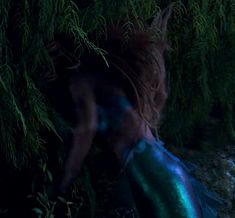 a woman in blue and green dress standing next to a body of water at night