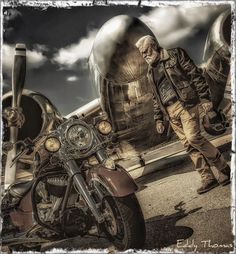 a man standing next to a parked motorcycle in front of an old style plane on the ground