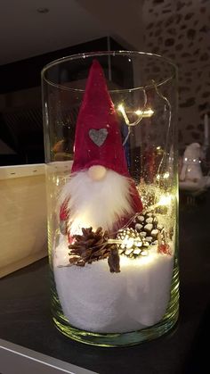 a glass jar filled with snow, pine cones and an elf's hat sitting on top of a table