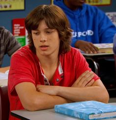 a boy sitting at a desk with his arms crossed