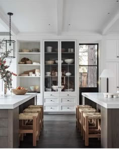 an open kitchen with white cabinets and wooden stools in the center, filled with dishes