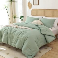 a bed with green sheets and pillows in a room next to a plant on the floor