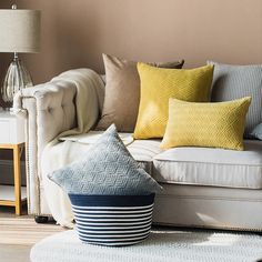 a white couch with yellow and blue pillows on it in a living room next to a lamp