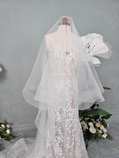 the back of a wedding dress with a veil on it and flowers in the background