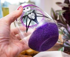 a hand holding a glass filled with purple sprinkles and a jack skellingy face on it