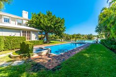 an outdoor swimming pool surrounded by lush green grass and trees with a house in the background