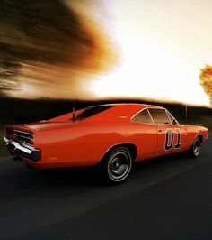 an orange muscle car driving down the road in front of a tree at sunset or dawn