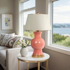 a pink vase sitting on top of a white table next to a lamp in a living room