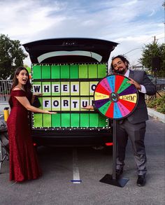 a man and woman standing in front of a wheel of fortune truck with a colorful wheel