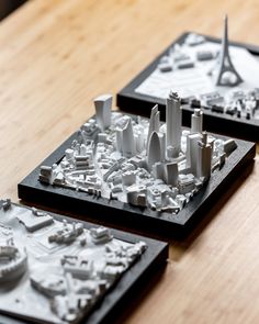 two models of city buildings are shown on a wooden table, with one model in the foreground