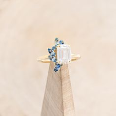 a ring with an emerald and blue topazte surrounded by small diamonds on a wooden stand