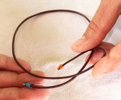 two hands are holding a brown cord that is connected to an orange and blue bead