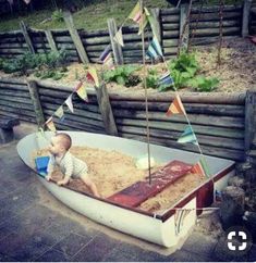 a baby sitting in a boat made out of sand with flags flying from it's sides