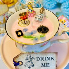 there is a tea cup with various items in it on the plate next to a sign that says drink me