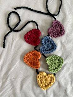 four crocheted hearts hanging from a black string on a white sheet with a knot in the middle