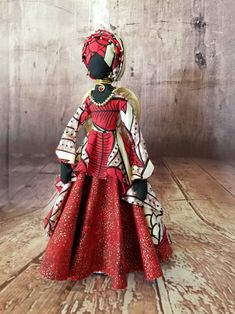 a red and white doll is standing on a wooden floor wearing a dress with gold accents